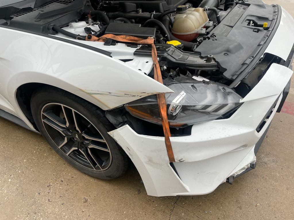 White Mustang with its front bumper removed during body repair at Sam’s