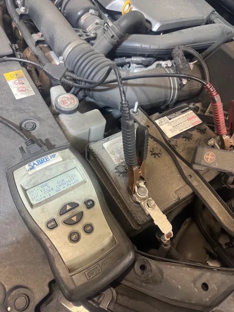 A battery tester connected to a car battery at John's Auto Care