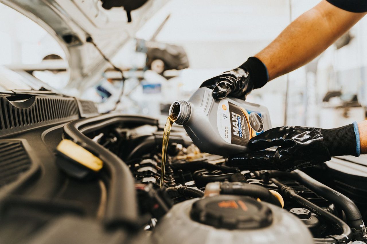 Gloved hands pouring motor oil into a car engine
